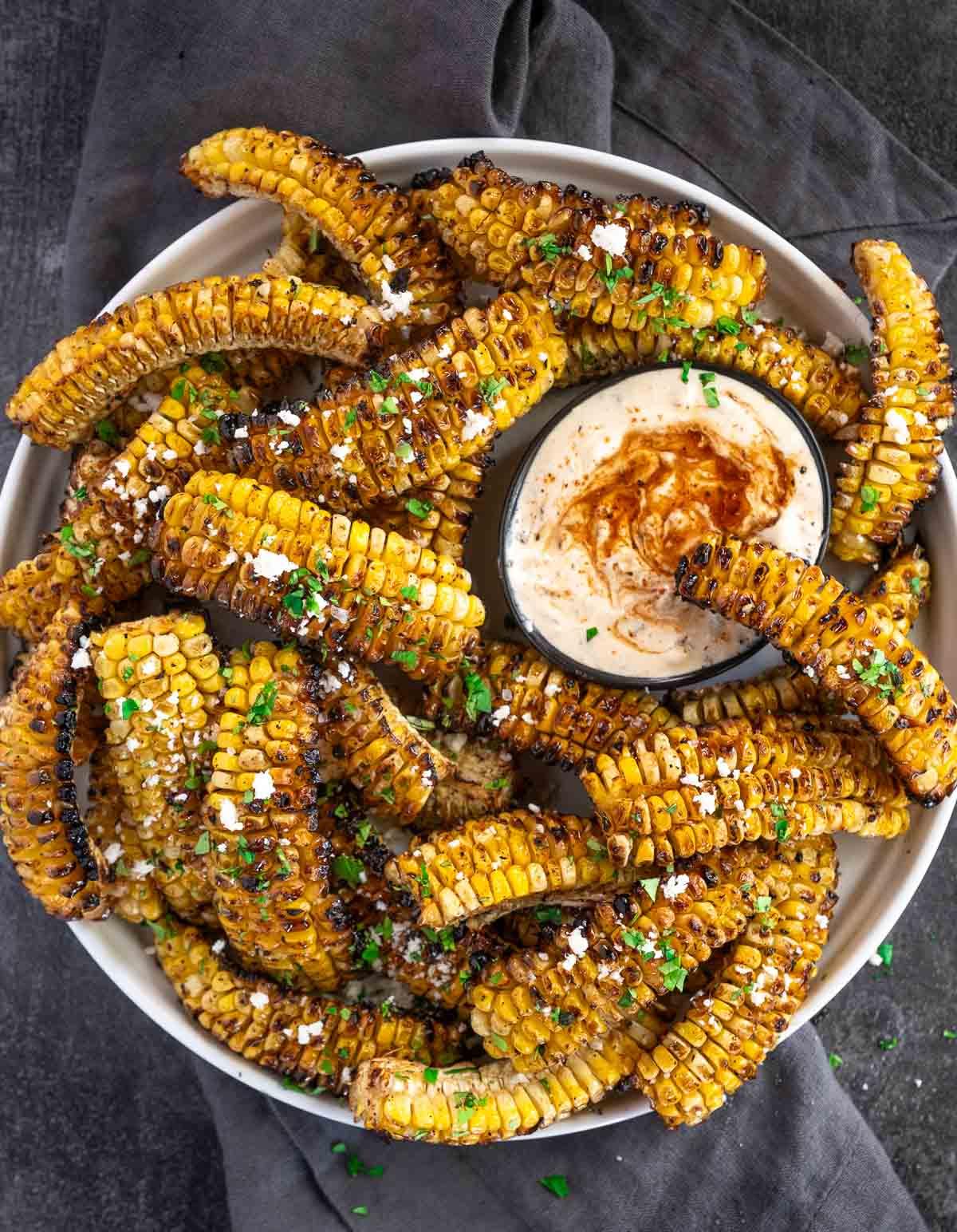 Ricetta Facile di Costine di Mais 2 Costine di Mais Grigliate su un piatto da portata con una ciotola di salsa per costine di mais