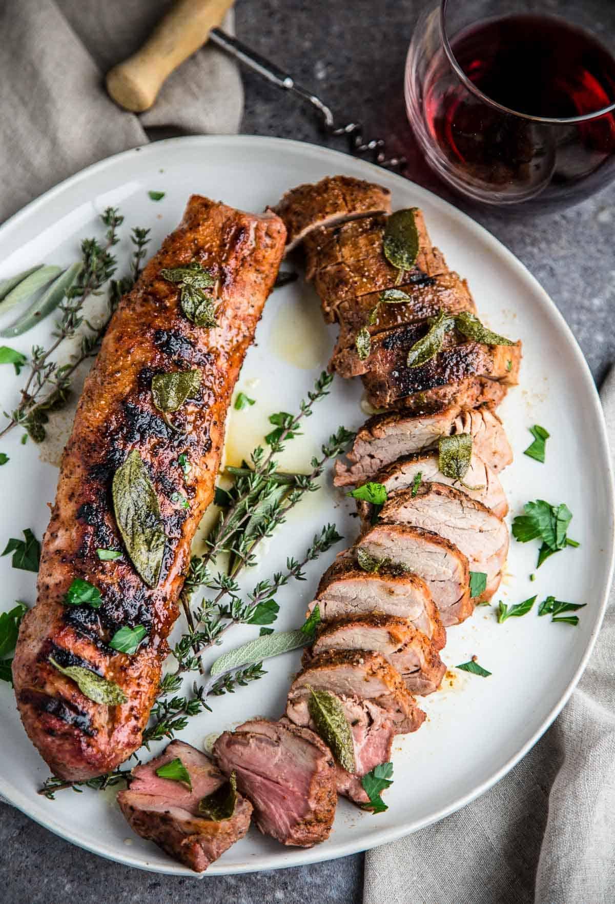 **Filetto di maiale alla griglia con salsa al burro e salvia fritta** 2 Filetto di Maiale Grigliato condito con salsa al burro e salvia fritta su un piatto da portata con un bicchiere di vino rosso.