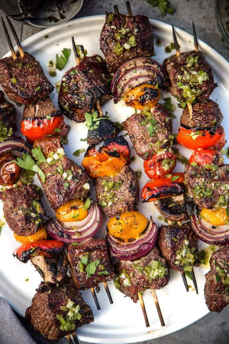 Spiedini di Manzo con Chimichurri al Jalapeño e Prezzemolo 2 Spiedini di Manzo con Marinatura alla Birra e salsa Chimichurri al Prezzemolo e Jalapeño su un piatto.