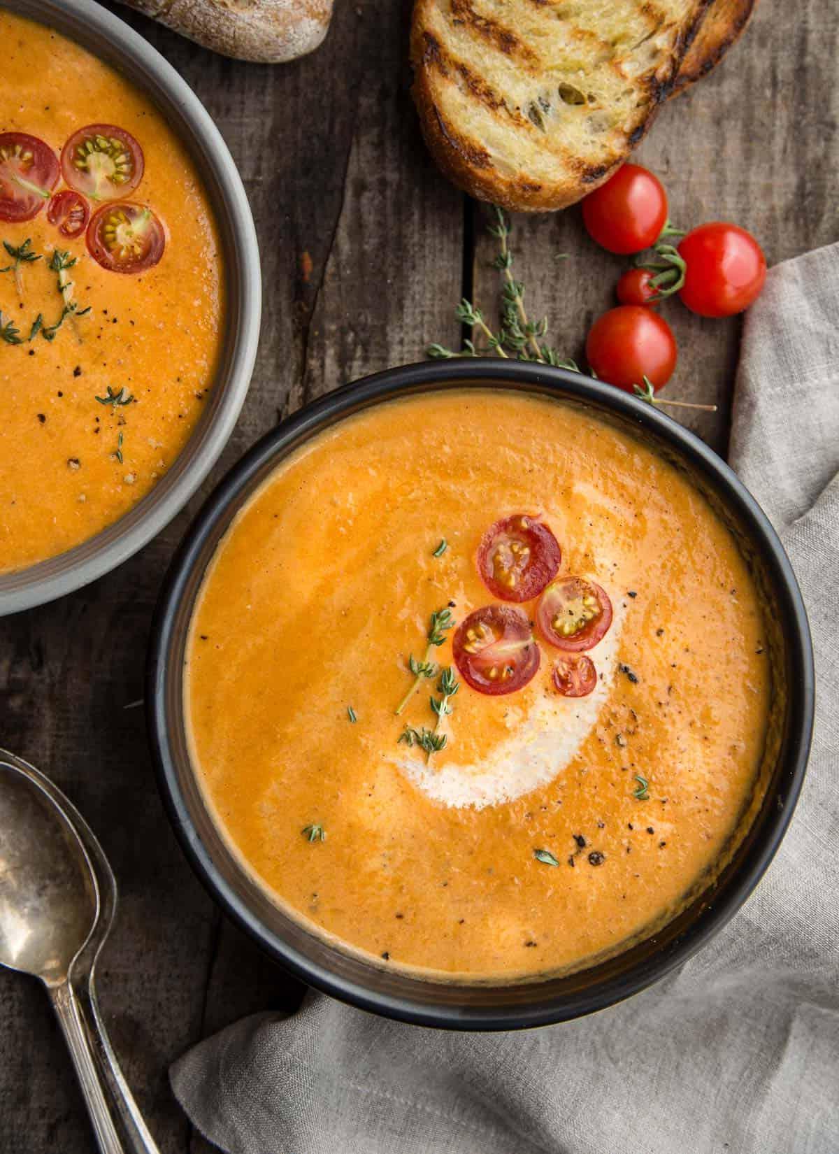 Vellutata di Pomodoro Affumicato 2 Una ciotola di bisque di pomodoro affumicato guarnita con pomodorini freschi e una fetta di pane tostato a lato.