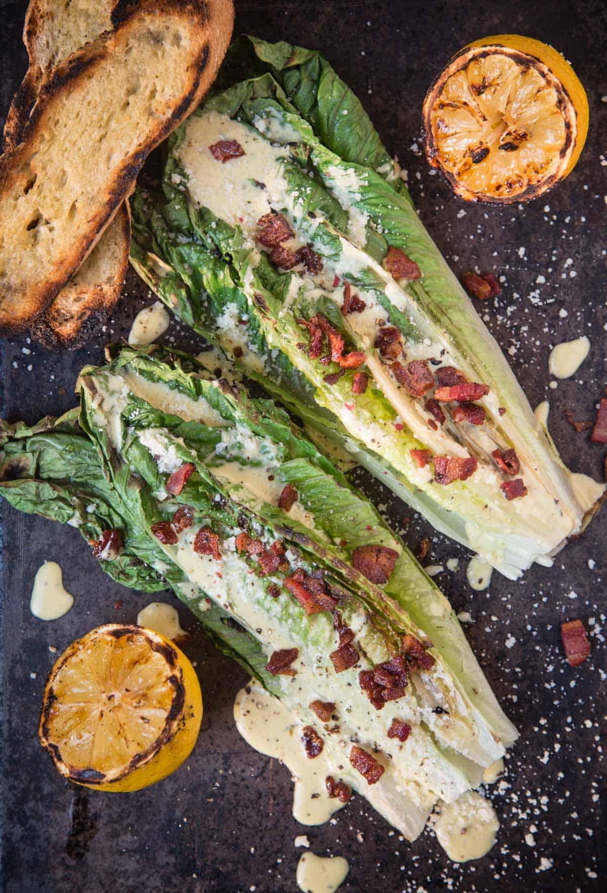 Insalata Caesar di Lattuga Romana Grigliata 2 Insalata Caesar con lattuga romana grigliata su un piatto da portata con limone grigliato e pane tostato