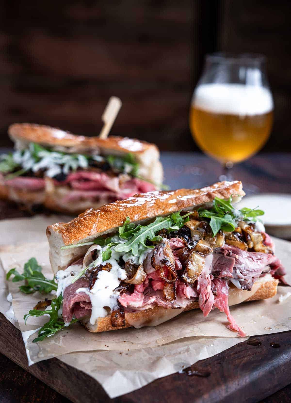 Panini di Costolette di Manzo Prime Rib su carta da forno su un tagliere con una birra.