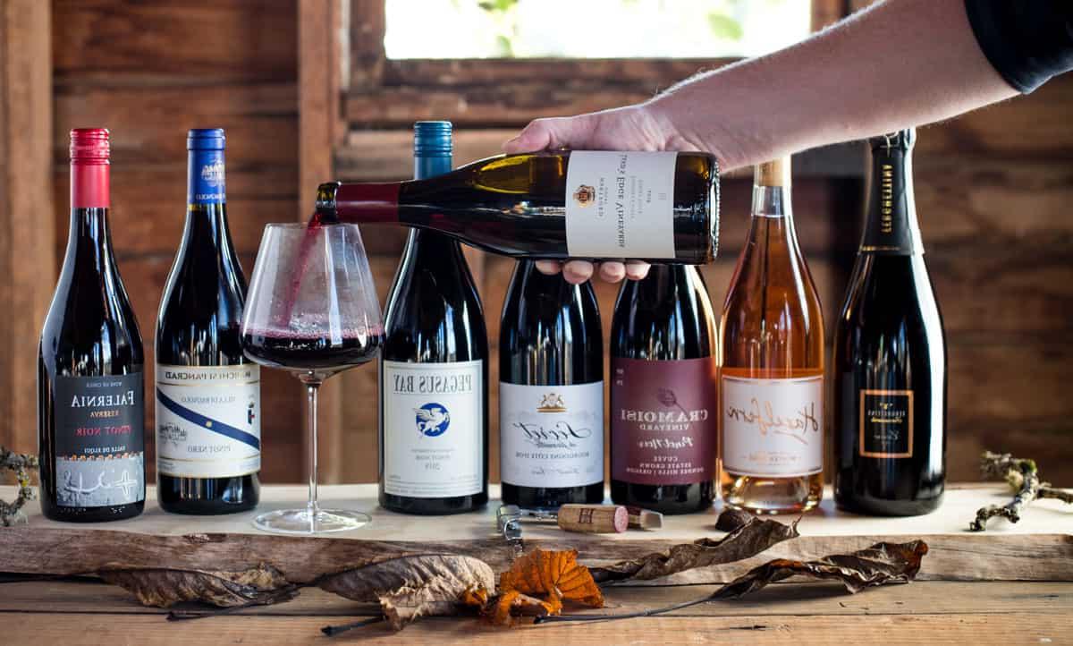 Guida al Pinot Noir 2 Una bottiglia di Pinot Nero viene versata in un bicchiere, con diverse bottiglie di Pinot Nero di stili diversi sullo sfondo.