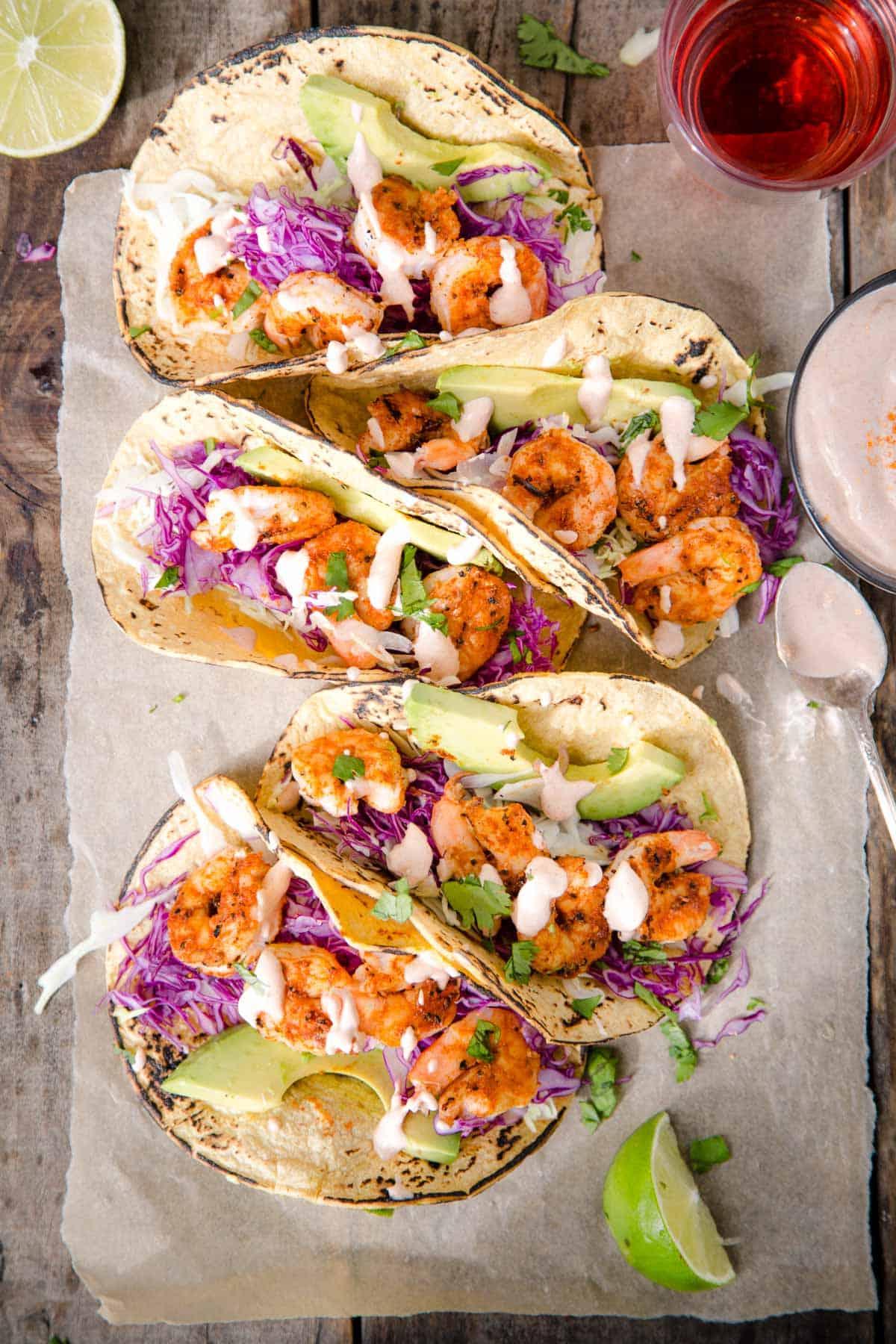 Tacos di Gamberi alla Griglia con Crema al Lime 2 5 Tacos di gamberi alla griglia su un piatto di legno con un bicchiere di vino rosato