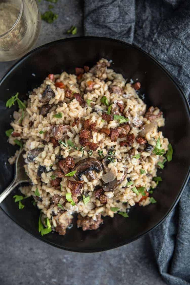 Risotto con Salsiccia Affumicata e Funghi 2 Una ciotola di Risotto con Salsiccia Affumicata e Funghi con un bicchiere di vino.