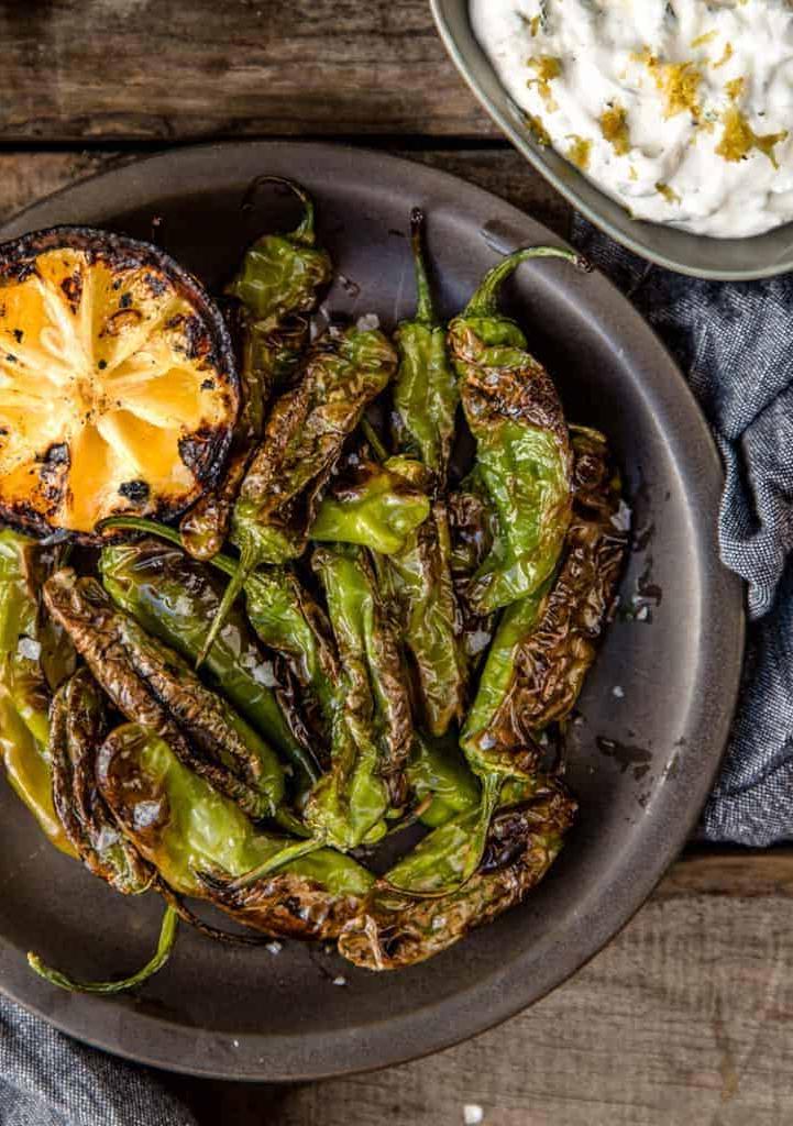 Peperoni Shishito Grigliati con Salsa di Yogurt al Limone per Intingere 2 Peperoni Shishito grigliati su un piatto con mezzo limone grigliato e salsa allo yogurt al limone