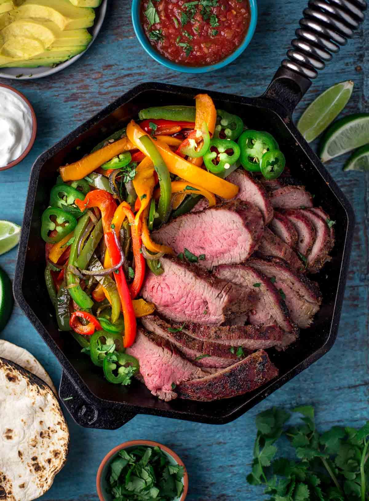 Ricetta Facile di Fajitas di Punta di Fianchetto Grigliata 2 Fette di Tri-Tip con cipolle e peperoni in una padella per fajitas.