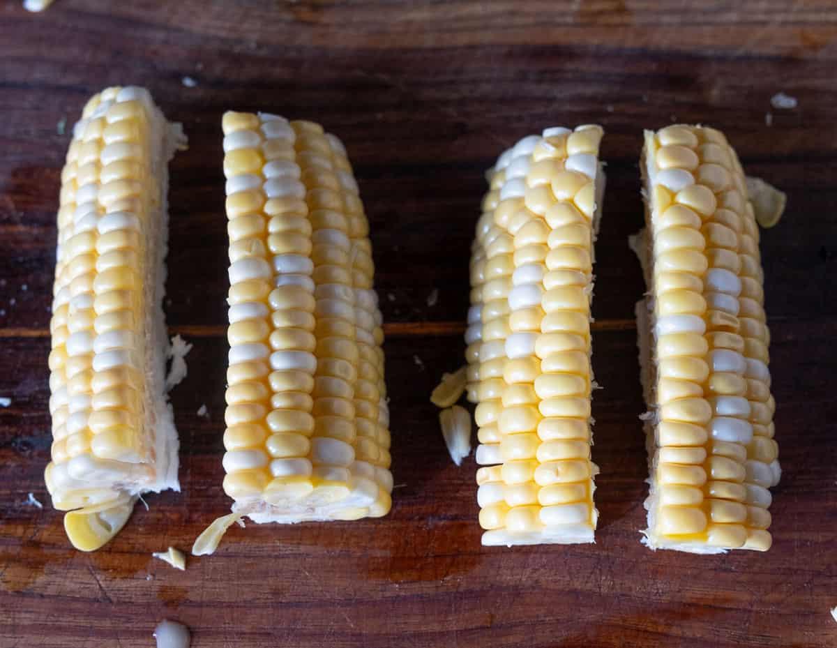 Ricetta Facile di Costine di Mais 12 Spighe di mais tagliate a quarti in preparazione per le costine di mais su un tagliere.