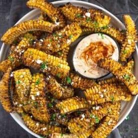 Ricetta Facile di Costine di Mais 18 Costine di Mais con salsa di accompagnamento su un piatto cosparse di formaggio cotija.