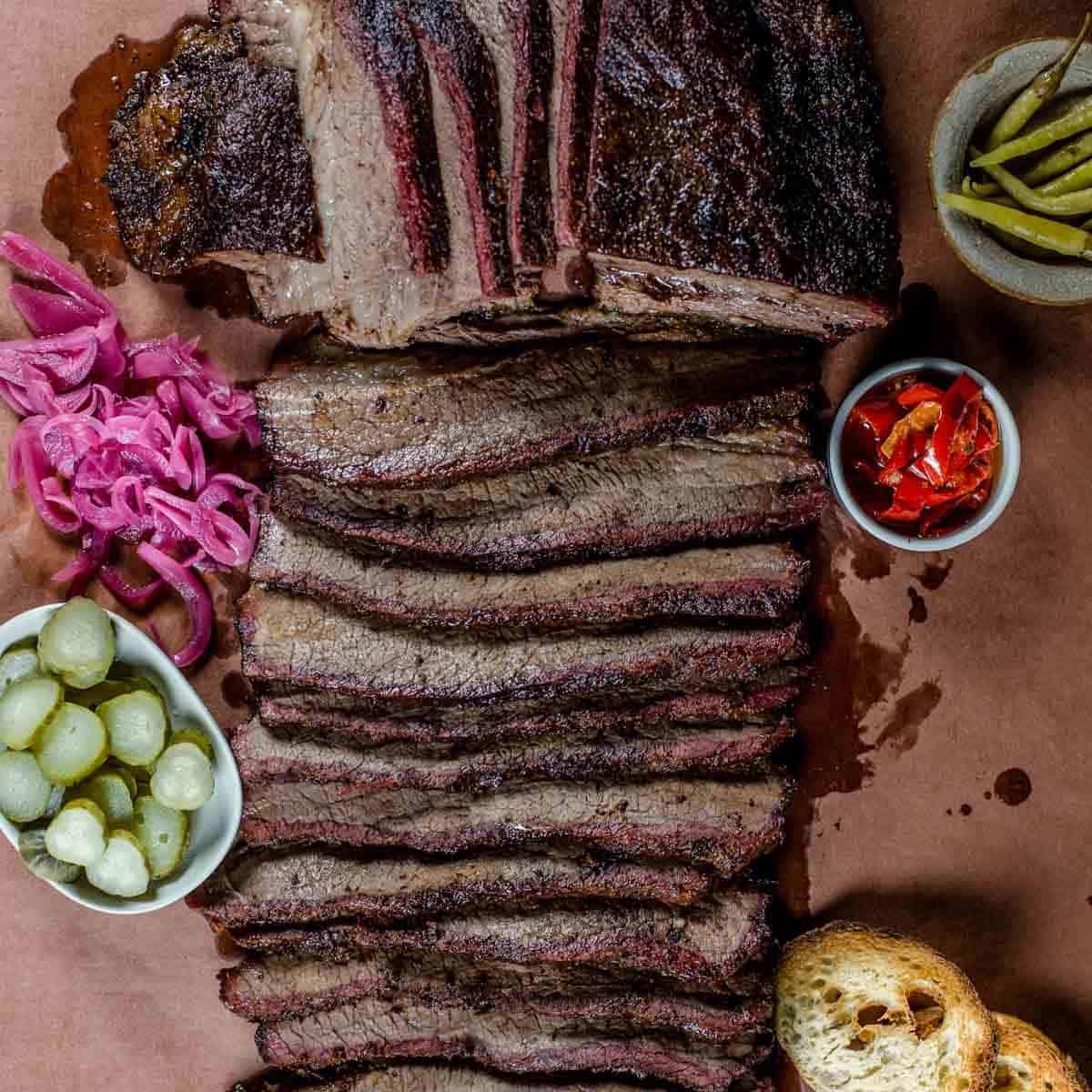 Migliori Tecniche e Ricette di Barbecue da Padroneggiare 18 Brisket affumicato affettato su carta da macellaio con verdure sottaceto.