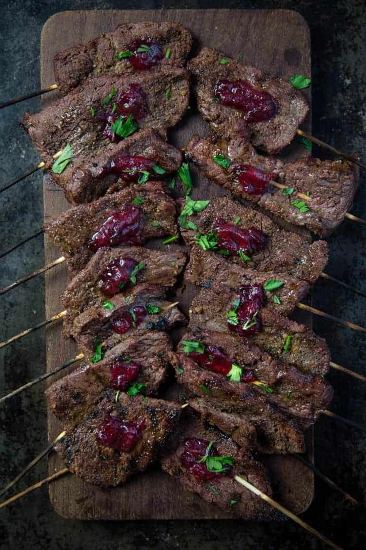 Spiedini di manzo su un tagliere con salsa di mirtilli rossi.