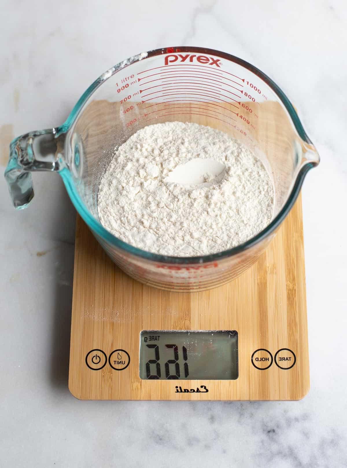 Strumenti Essenziali per la Pizza Fatta in Casa 3 Una bilancia digitale che misura la farina in un piatto di vetro per una preparazione accurata dell'impasto della pizza