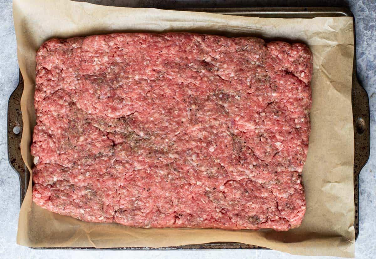 Un rettangolo di carne macinata pronto per i slider su una teglia rivestita di carta forno.