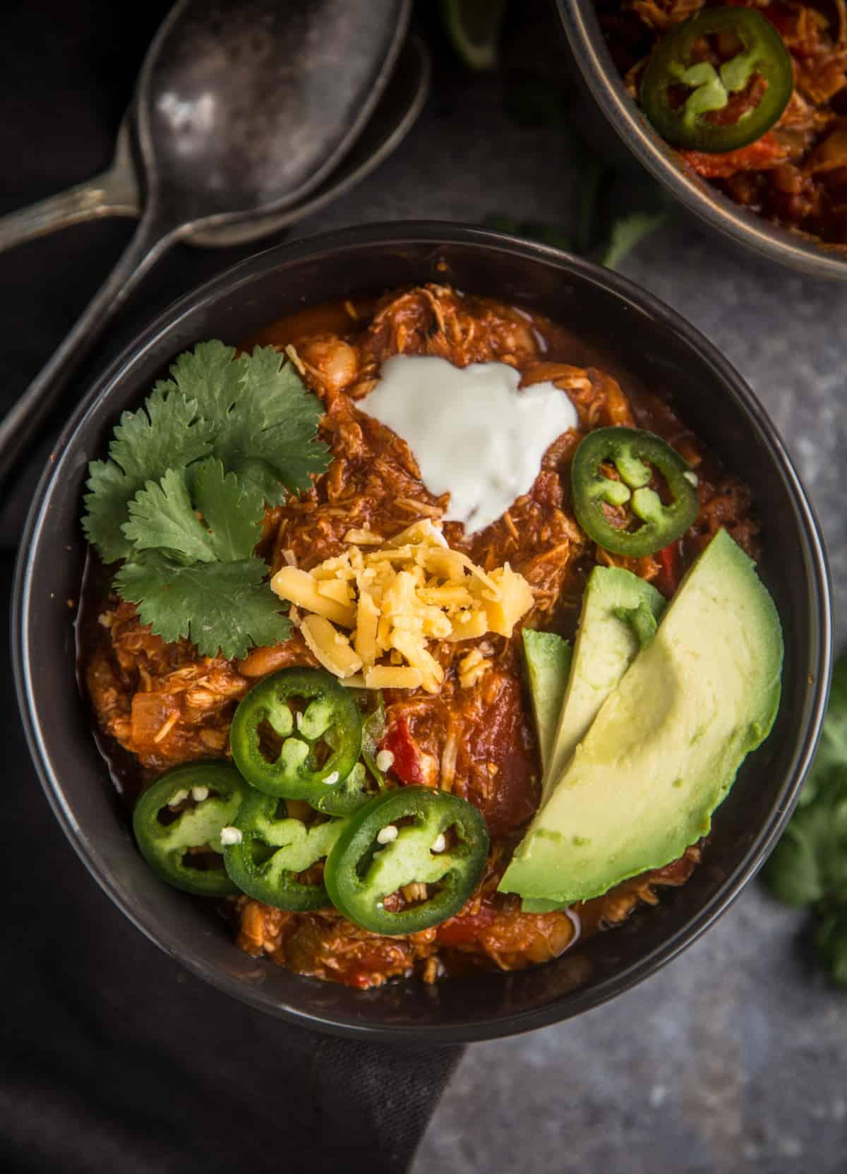 Ricetta Chili di Pollo Affumicato Facile 4 Una ciotola di chili di pollo affumicato facile, guarnita con avocado, formaggio e jalapeño.