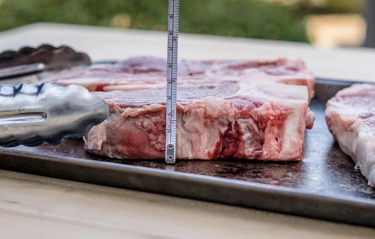 Bistecca Porterhouse Alla Griglia – Cottura Inversa 4 Una bistecca cruda vista lateralmente con un righello che mostra uno spessore di 1 pollice e mezzo.