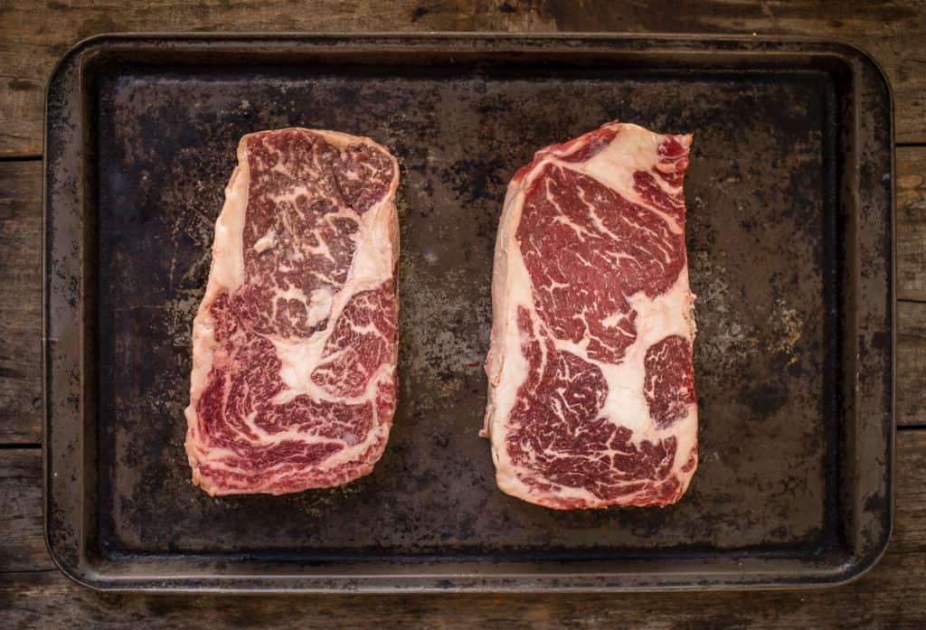 Choice vs Prime – Qual è la qualità migliore per grigliare e affumicare? 4 Ribeye Prime marmorizzato a sinistra e Wagyu americano a destra, non conditi.