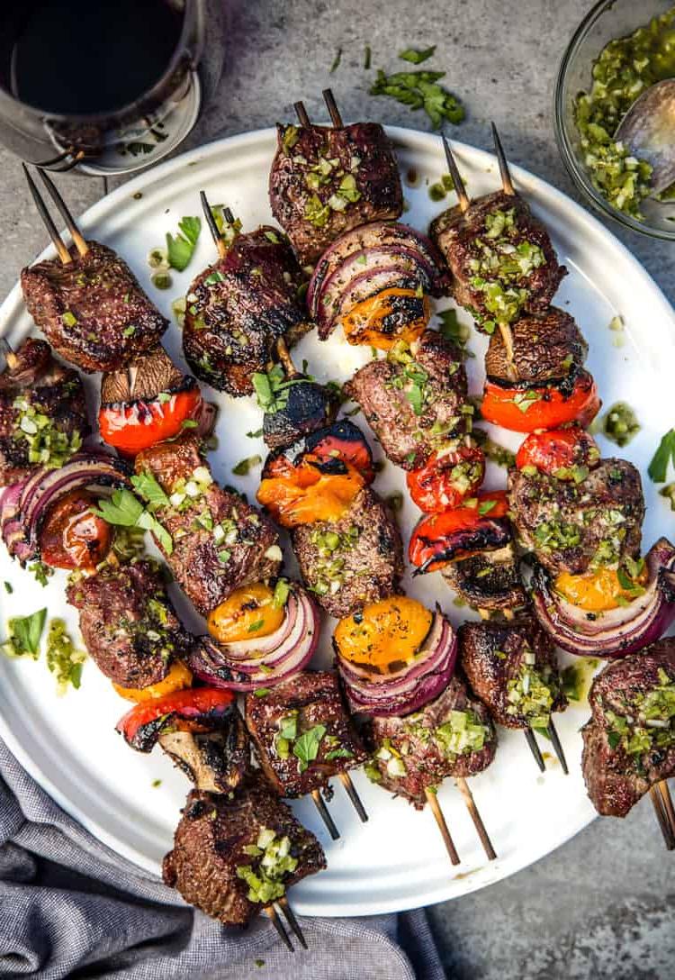 Spiedini di Manzo con Chimichurri al Jalapeño e Prezzemolo 5 Spiedini di Manzo (Kebabs) su un piatto rotondo bianco conditi con una salsa chimichurri al jalapeño