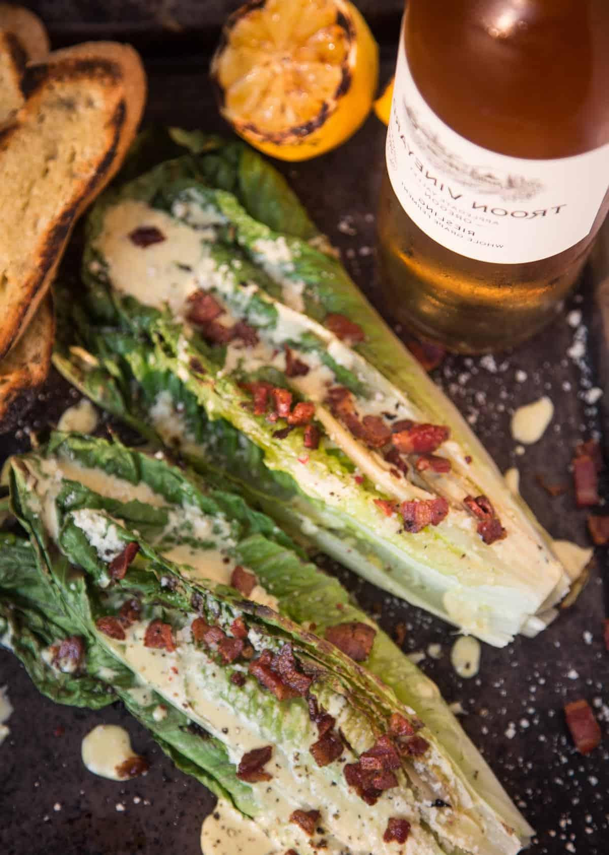 Insalata Caesar di Lattuga Romana Grigliata 5 Insalata Caesar grigliata su un vassoio con una bottiglia di vino