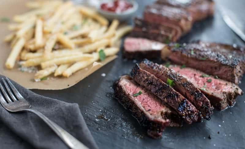 Ricetta per Bistecca NY Strip Grigliata con Rub al Caffè. Facili e deliziose bistecche New York Strip, marinate in un mix di caffè e vino e grigliate alla perfezione. Bistecca al caffè affettata con patatine fritte croccanti.