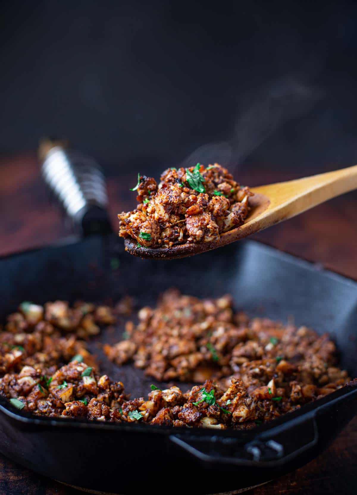 Ricetta di Chorizo Vegetariano con Cavolfiore 5 Un cucchiaio di legno di Chorizo di Cavolfiore guarnito con prezzemolo preso da una padella di ghisa.