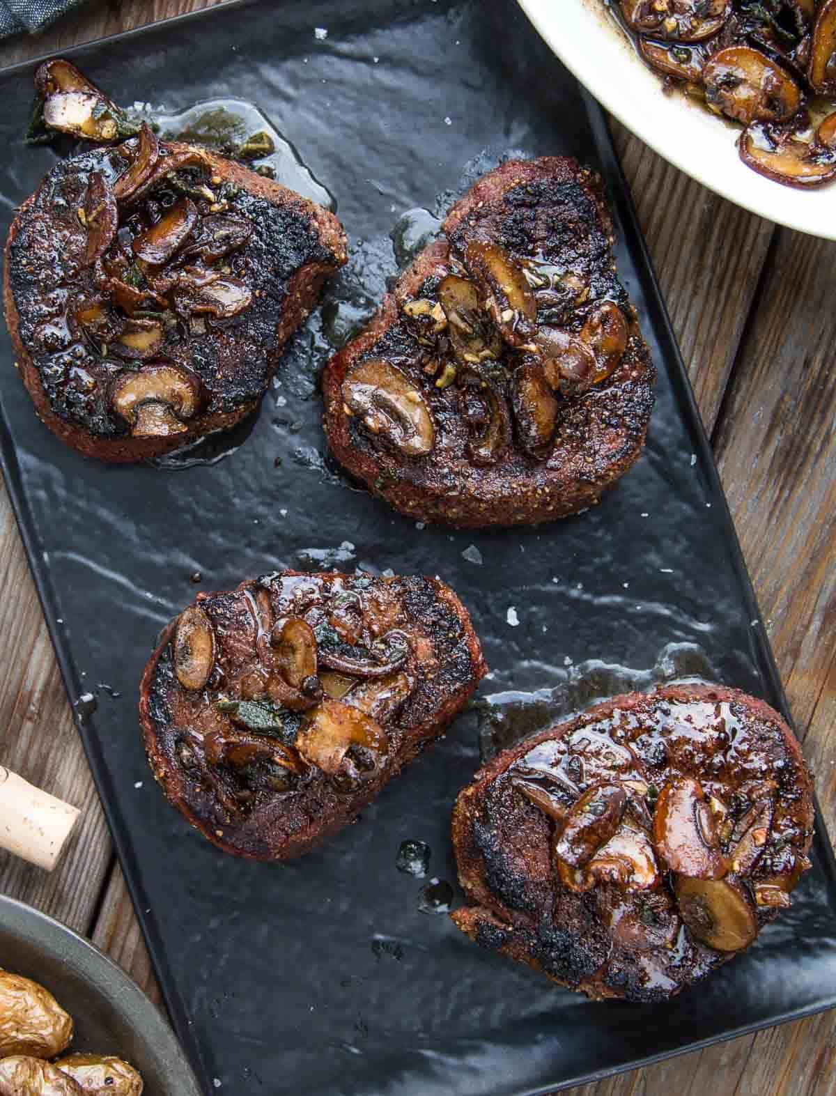 **Filetto di Manzo alla Griglia con Salsa ai Funghi e Burro Nocciola** 6 Filetti mignon alla griglia con salsa ai funghi al burro nocciola su un piatto da portata.