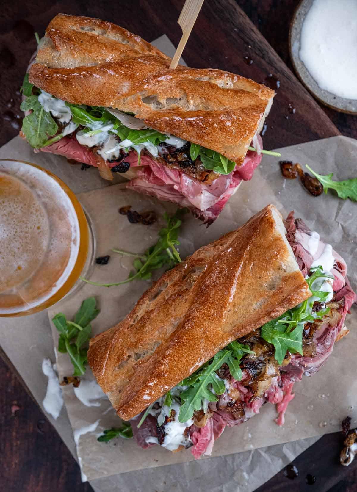 Foto dall'alto di due panini di prime rib steak su carta da forno con una birra a lato.