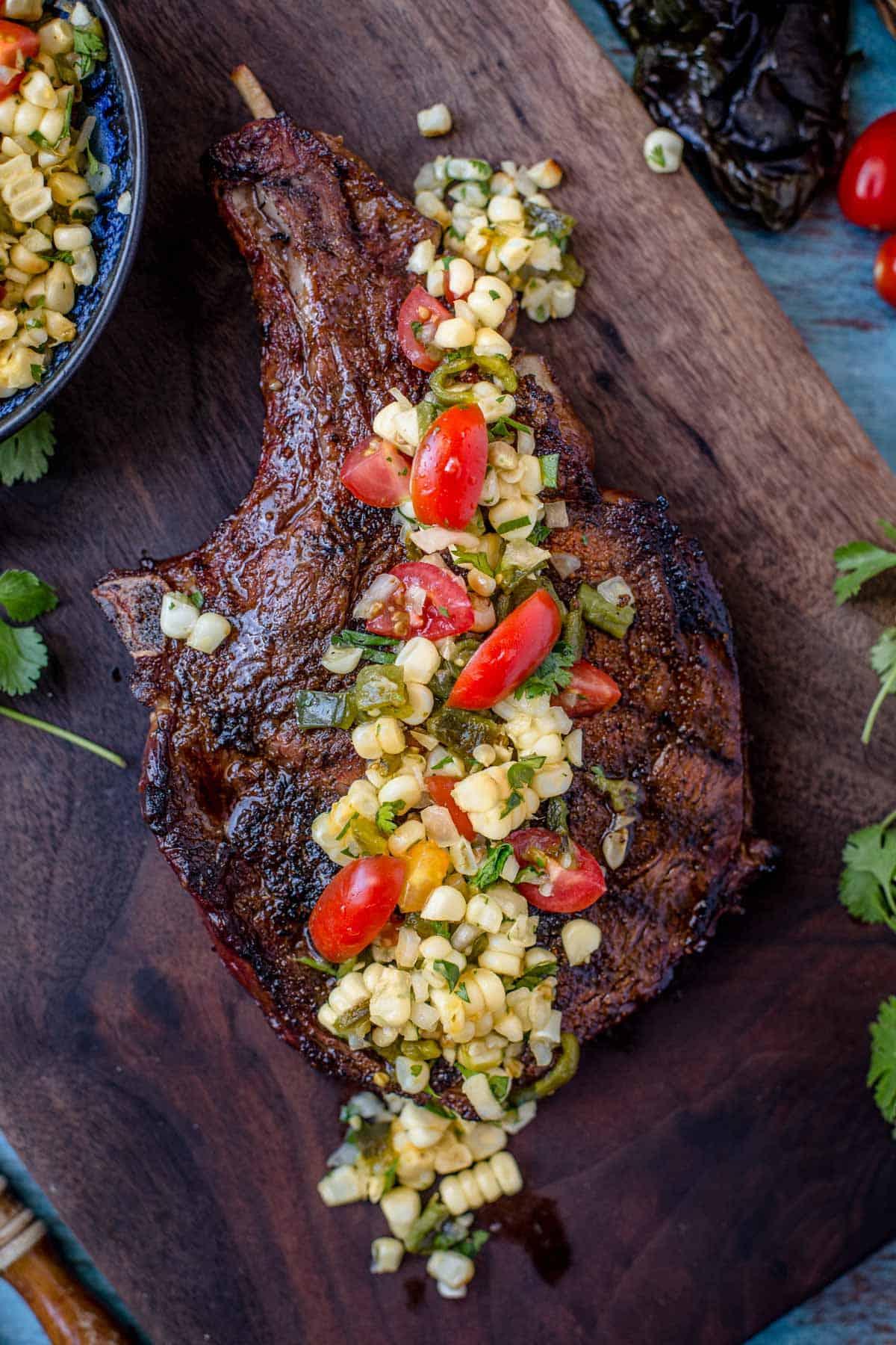 Una bistecca tomahawk guarnita con salsa di mais su un tagliere.