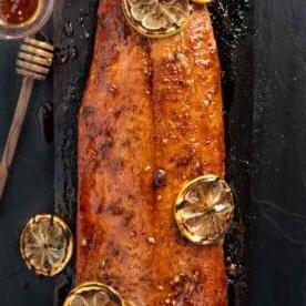 Salmone Grigliato al Miele Piccante 7 Un'immagine quadrata di salmone al miele piccante su un piatto di ardesia glassato con miele piccante e guarnito con limoni grigliati.