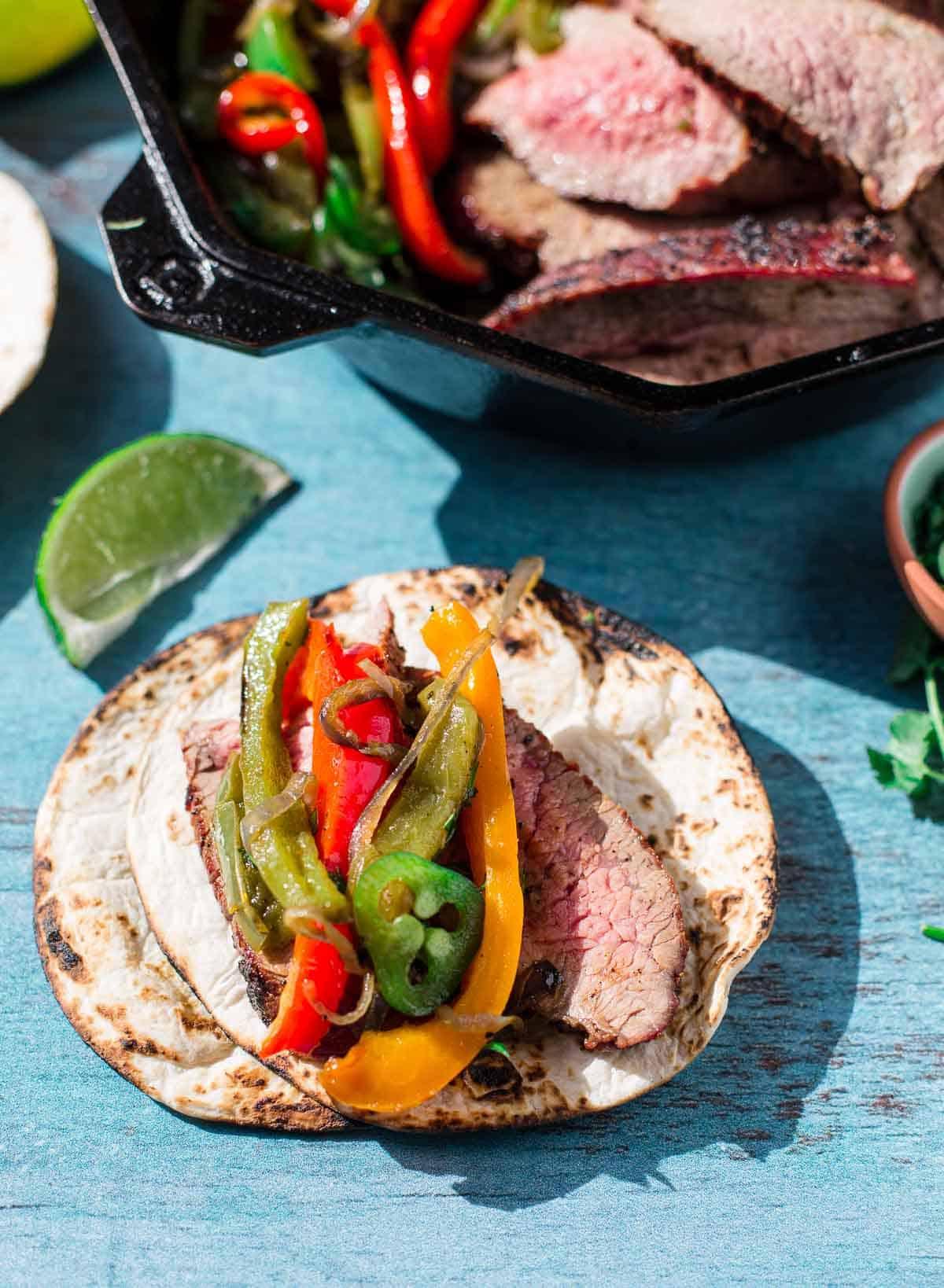 Ricetta Facile di Fajitas di Punta di Fianchetto Grigliata 7 Fajitas di Tri-Tip con contorni e condimenti su un tagliere.