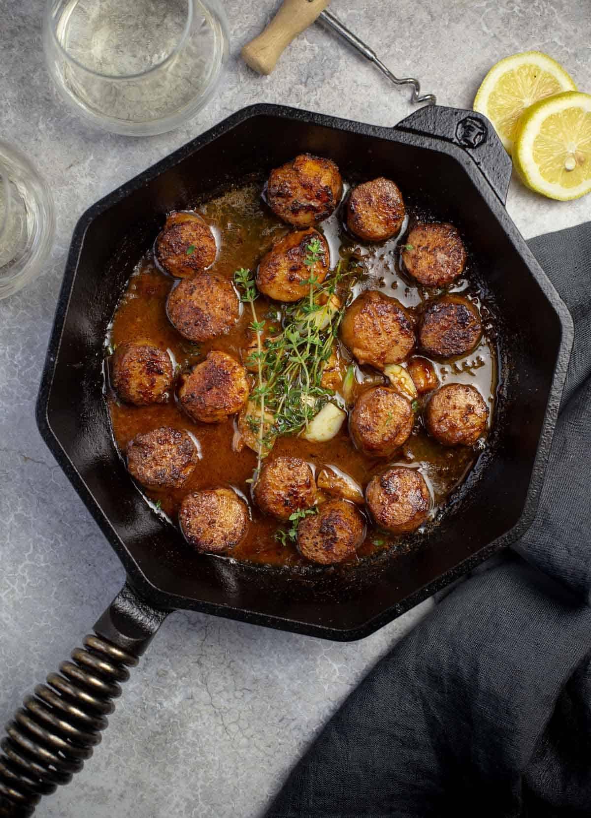 Capesante grigliate in una padella di ghisa con salsa al burro, vino bianco ed erbe aromatiche