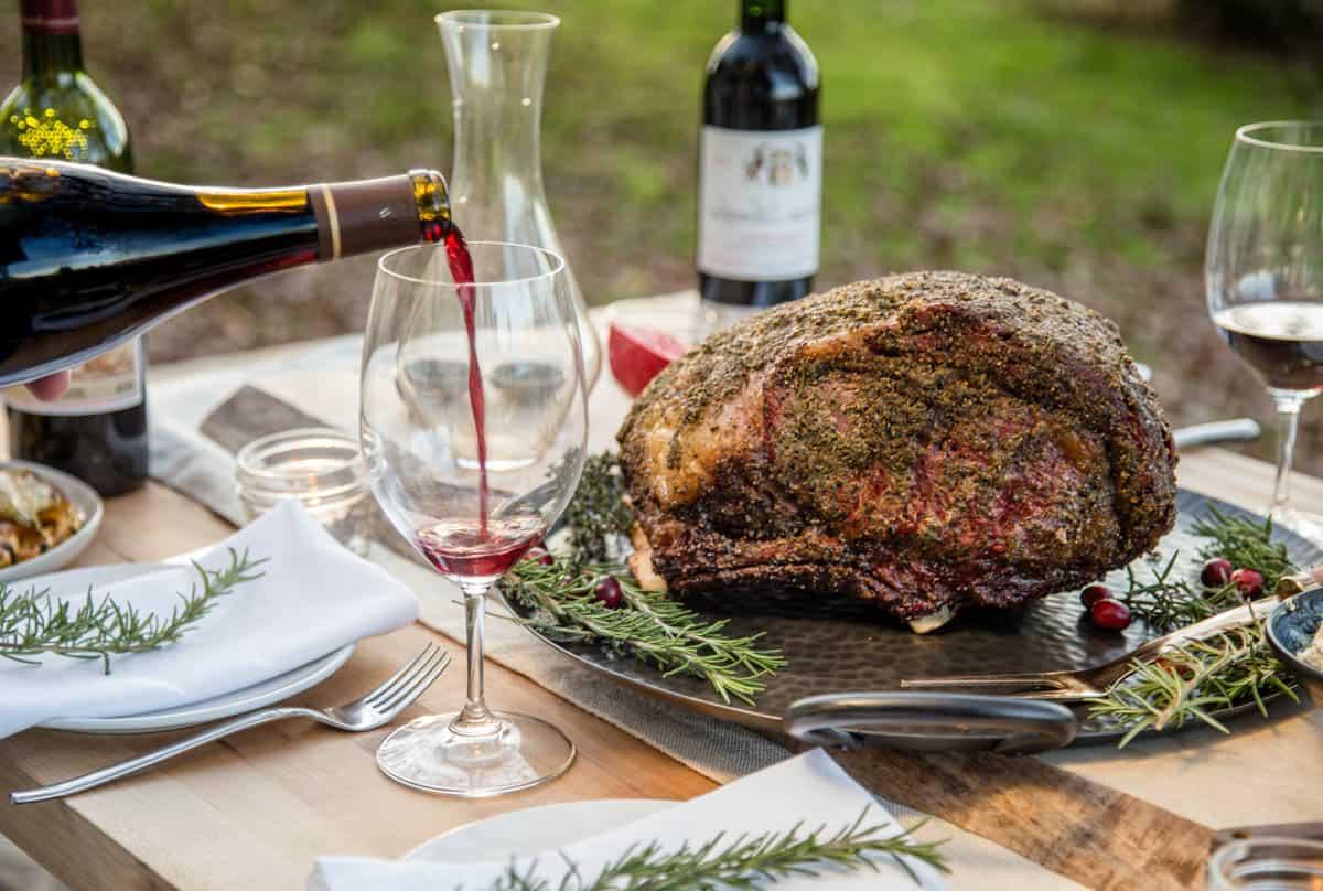 La Migliore Costata di Manzo Affumicata (Ricetta + Video) 8 Vino rosso versato in un bicchiere su una tavola apparecchiata per una cena festiva.