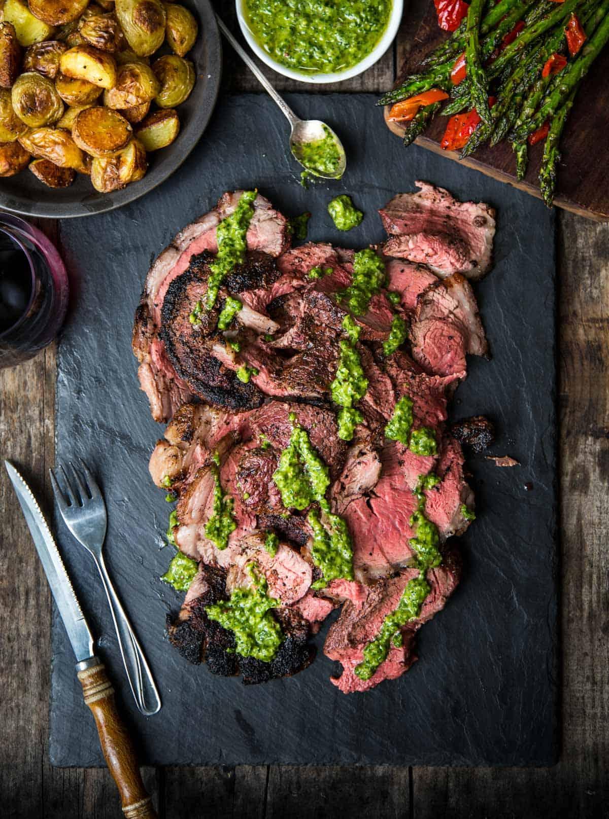Fette di Bistecca di Picanha alla griglia condite con salsa chimichurri su un piatto nero di ardesia.