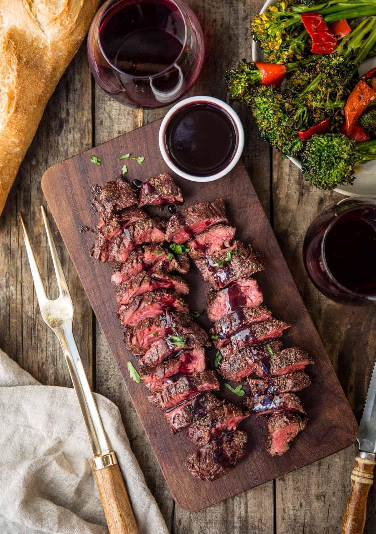 Diaframma di Manzo alla Griglia con Glassa al Pinot Nero e Marionberry 2 Bistecca di diaframma alla griglia su un piatto di legno, ricoperta di salsa di riduzione al vino e due bicchieri di vino
