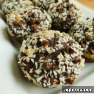 A perfectly baked muffin, golden brown with visible coconut flakes and chocolate chips on top.