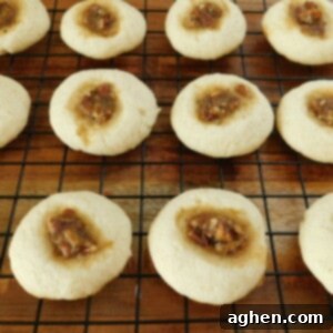 Buttery Pecan Thumbprint Delights 2 A freshly baked Pecan Thumbprint Cookie with a slightly golden crust and a glistening pecan filling, resting on a cooling rack.