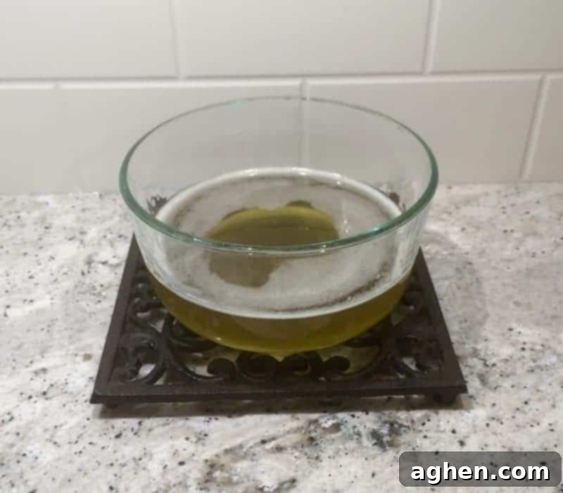 Melted shea butter and coconut oil mixture in a glass bowl, appearing clear, smooth, and liquid after heating.