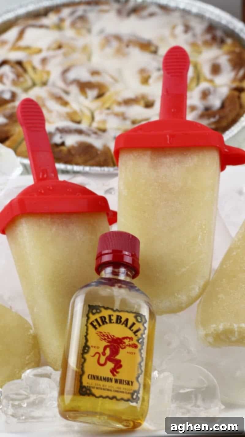 Fireball Cinnamon Roll Booze Pops 4 Fireball Whiskey cinnamon roll ice pops served on platter of ice with tray of cinnamon buns in the background and bottle of fireball cinnamon whiskey next to them