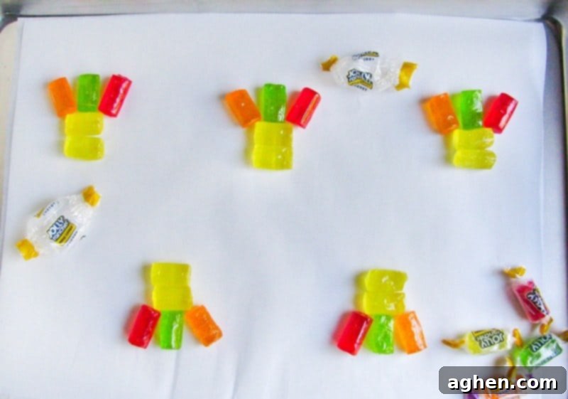 Unwrapped Jolly ranchers arranged on lined cookie sheet with two yellow candies on top of one another horizontally and red, orange, and green candies standing up vertically on top to look like feathers.