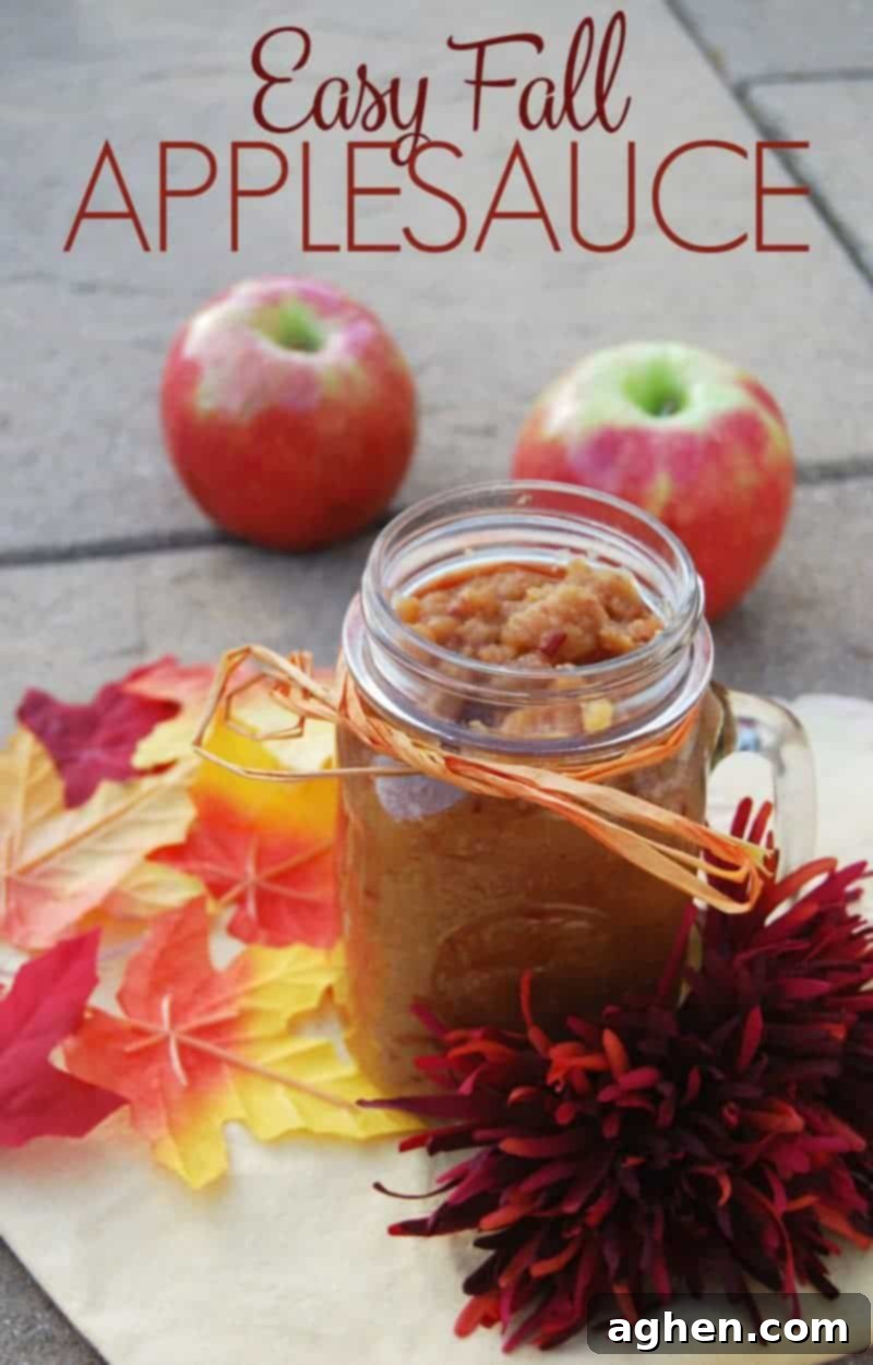 Easy Fall Applesauce Recipe Pin. Homemade applesauce in a glass jar, garnished with a cinnamon stick and fresh apple slices, set against a rustic wooden background with autumn leaves.
