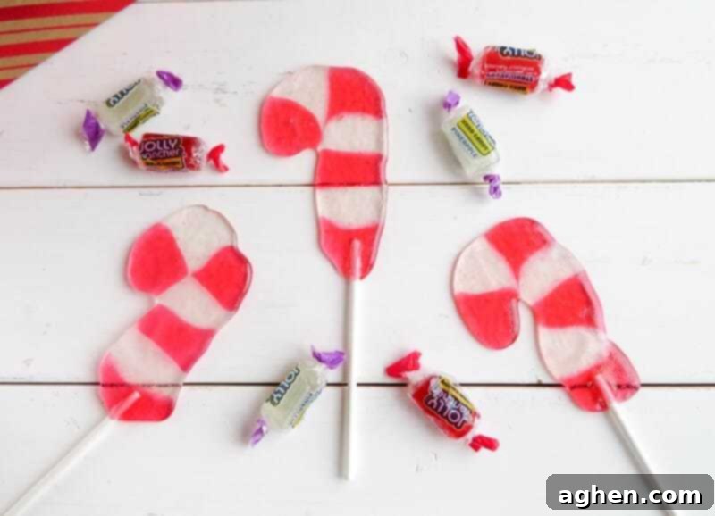 Candy cane shaped suckers on white wood background with strawberry and pineapple jolly rancher candies scattered around.