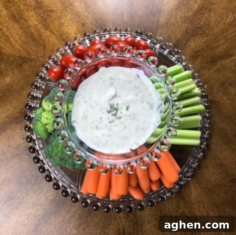 A beautifully arranged platter featuring a bowl of creamy bacon ranch dip, surrounded by an appetizing array of fresh-cut vegetables like carrots, celery, bell peppers, and cucumber slices, perfect for healthy dipping.
