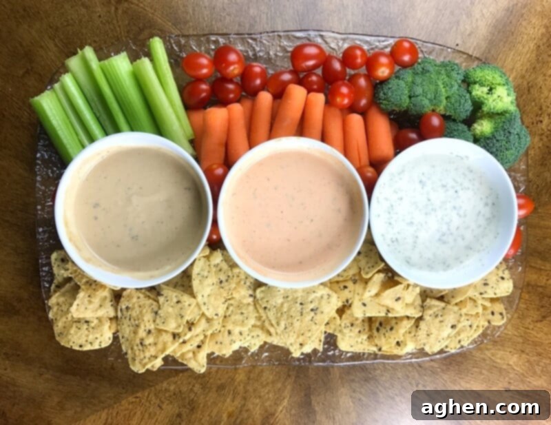 A vibrant appetizer platter showcasing three distinct ranch-based dips alongside crispy tortilla chips and an abundant selection of fresh, colorful vegetables, illustrating the versatility of ranch dressing.
