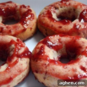 A close-up of a raspberry jam donut, showcasing the vibrant red jam filling on top.