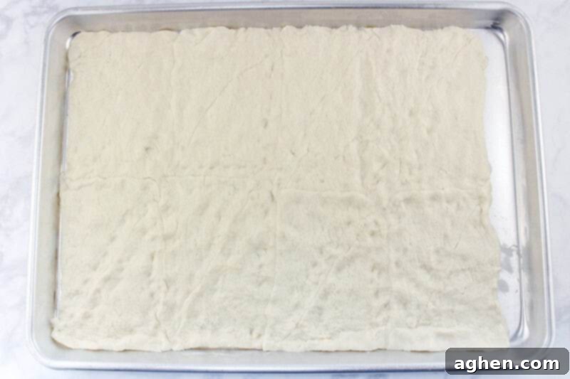 Crescent roll dough spread onto baking sheet, with seams pinched, ready for baking to create the pizza bar crust.