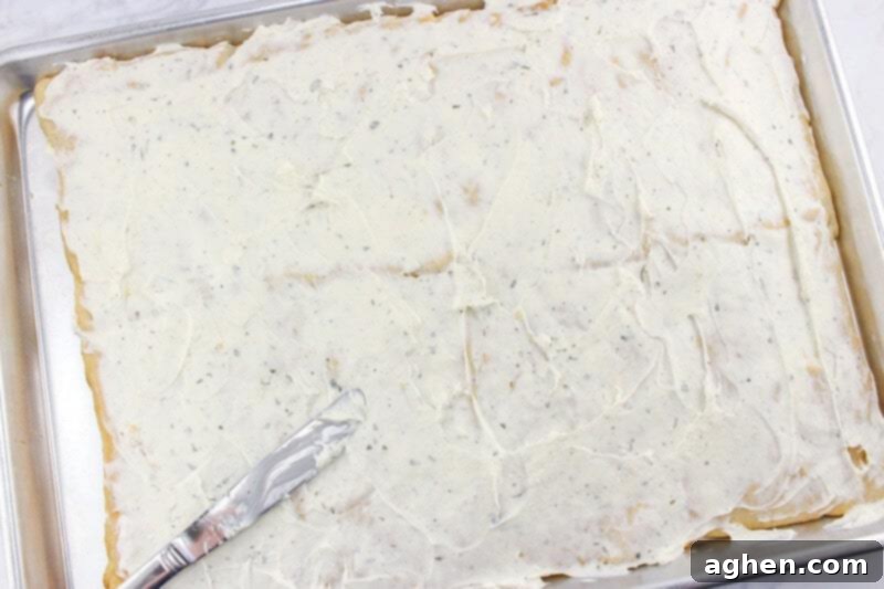 Cream cheese and ranch spread smoothly onto the cooled crescent roll crust, forming a delicious base for the vegetables.