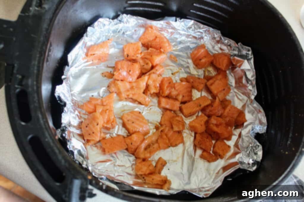 Diced salmon chunks marinating in an air fryer basket lined with foil, ready for cooking