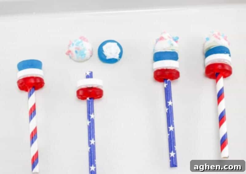 The process of assembling a 4th of July Firework Cupcake topper, showing red, white, and blue Life Savers being threaded onto a paper straw, with melted white chocolate on the final blue gummy ready to attach a Hershey Kiss.