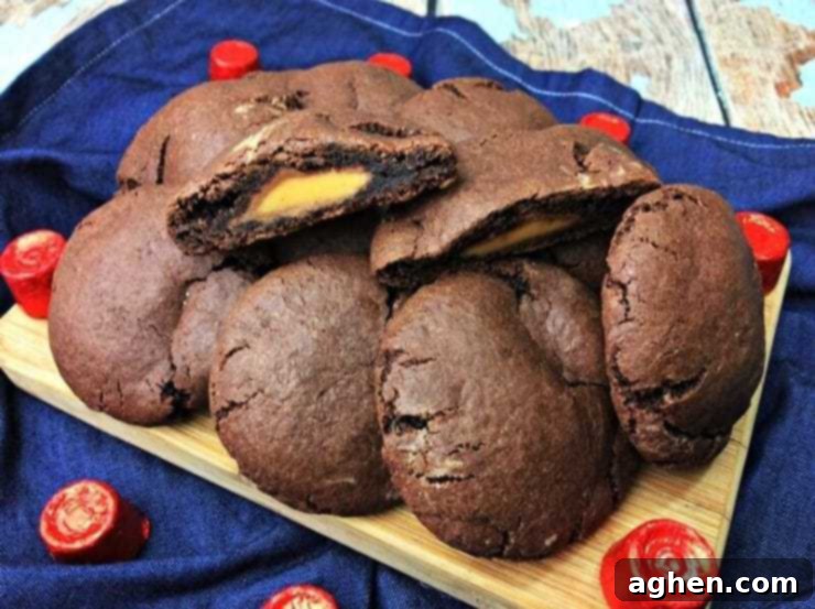 Rolo stuffed chocolate cookies piled on wooded cutting board with one cookie sliced in half to show the melted Rolo caramel inside.