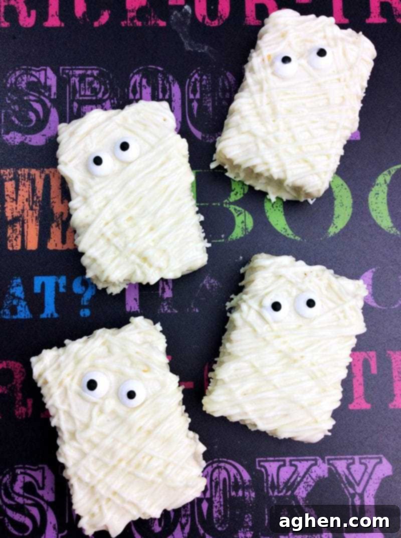Four Mummy Rice Krispie Treats decorated for Halloween with white chocolate 'bandages' and edible candy eyes.