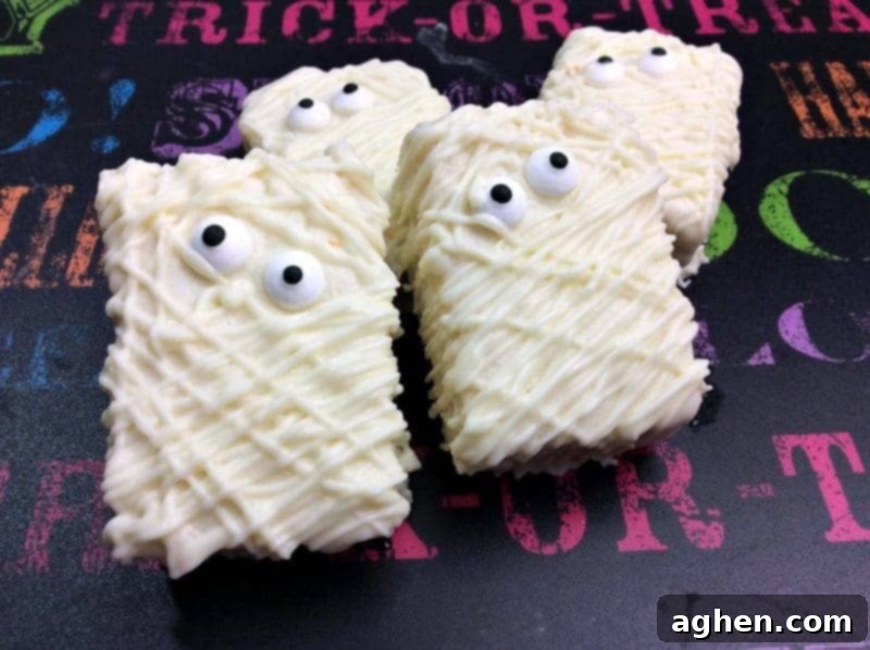 Close-up of a group of homemade Mummy Rice Krispie Treats, showcasing their edible candy eyes and white chocolate drizzled 'bandages'.